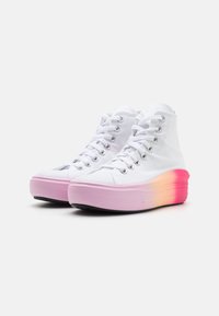 Weiße High-Top-Sneaker aus Canvas mit einer pinken bis orangefarbenen Farbverlaufsohle, ausgestattet mit metallischen Ösen und weißen Schnüren. Gummi-Zehenkappe und strukturiertes Außensohlenprofil.