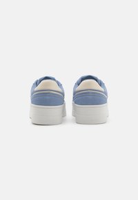 Sneakers in suede blu con suola in gomma bianca, caratterizzate da un elegante dettaglio crema sul tallone e da elementi di brand sul retro.