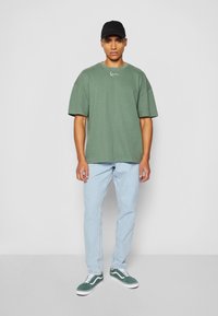Grønn oversized t-skjorte med kort erme, med en liten hvit logo. Kombinert med lyseblå jeans og grønne sneakers med hvite detaljer.