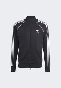 Svart zip-up jacka i sportigt tyg, med vita tre-rands detaljer på ärmarna och en broderad logotyp på bröstet.