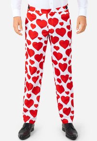 Biele nohavice s červeným srdcovým vzorom, vyrobené z ľahkej látky. Majú uzáver na gombík a čierne topánky.