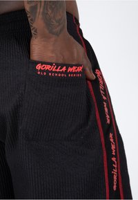 Schwarze strukturierte Shorts mit roten Akzenten. Verfügt über Seitentaschen und besticktes "GORILLA WEAR"-Label auf der Tasche und der Seitennaht.