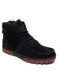 Black high-top boots made of suede and textile, featuring a faux fur collar. The rubber sole is brown with a textured grip pattern.