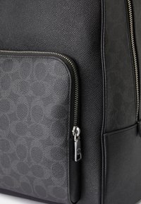 Mochila preta em pele com um acabamento texturizado, apresentando um bolso liso em cinza com impressão de logótipo, fechos de zíper prateados e pormenores mates.