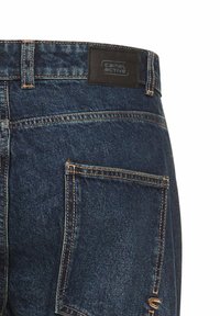 Denim jeans met een donkerblauwe wassing, voorzien van contrasterende stiksels, een rechthoekig zwart label en een achterzak met een subtiel logoontwerp.