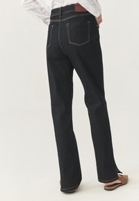 Jeans negre din denim cu croială evazată, talie înaltă, cusături contrastante aurii, două buzunare în spate și fente pe margine.