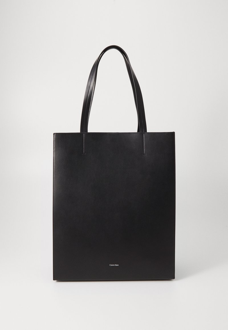 Sac à main en cuir noir avec deux poignées supérieures, forme rectangulaire plate, design minimaliste et marquage près du bas.