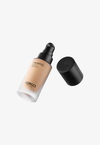 Base en una botella de vidrio transparente con tapa de bomba negra. El producto tiene un color bronceado claro y presenta un diseño de marca minimalista.