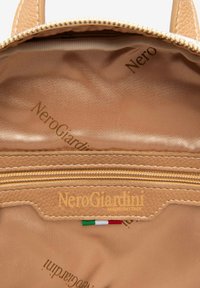 Brun läderryggsäckens inredning med dragkedjefack; har "NeroGiardini"-logotyp i guld och italienskt flaggdetalj. Slät textur, funktionell design.