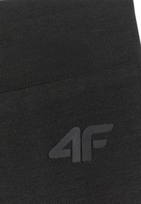 Gros plan d’un tissu noir texturé avec un logo "4F" en relief de couleur sombre assortie centré sur le matériau.