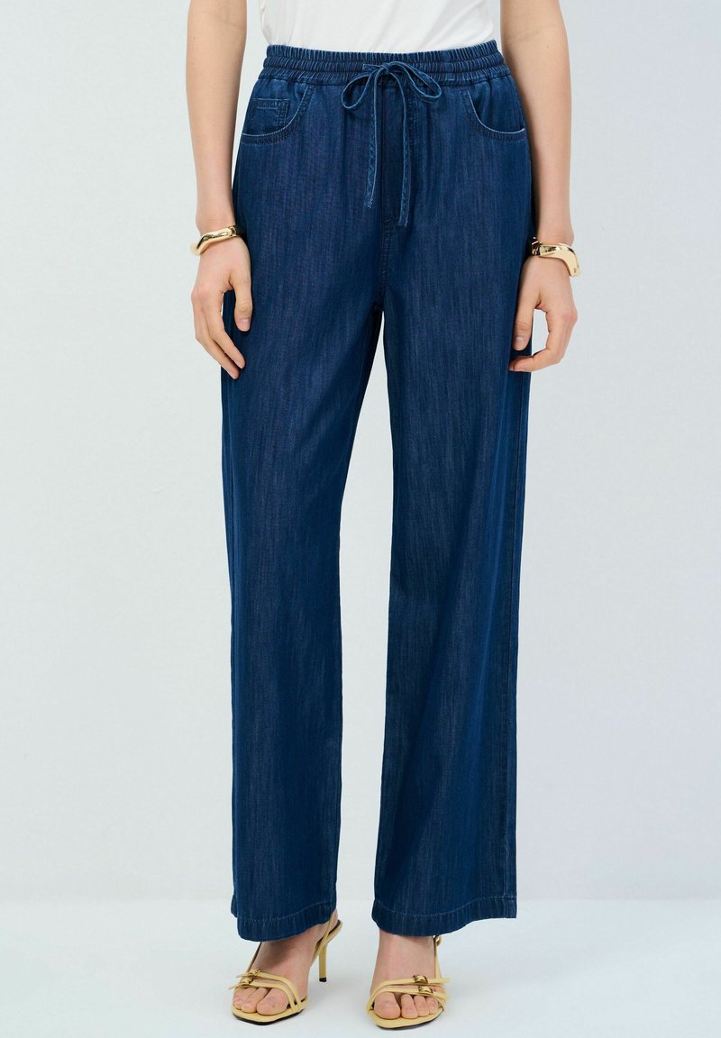 Pantalones de pierna ancha azul marino de mezclilla, con cinturilla elástica y cordón, dos bolsillos frontales y una textura suave.