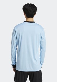 Ljusblå långärmad tröja i jersey med ribbad textur, svart krage och kontrasterande manschetter. Den har en avslappnad passform och inga framträdande logotyper.