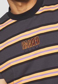 Grå t-shirt med vandrette striber i orange, lilla og sort. Har et centralt broderet logo "RAGGED JEANS" i orange og sort.