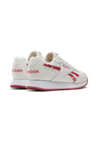 White sneakers with a textured leather upper, featuring red accents and a printed stripe on the side. Thick white and pink sole.