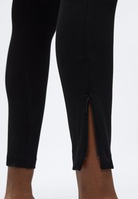 Sorte leggings med ankellynlås, glat tekstur, tæt pasform og kortet snit over anklen.