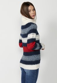 Pull en tricot avec un col haut et côtelé, présentant des rayures horizontales bleu marine, rouge, gris et crème, avec une finition douce et texturée.