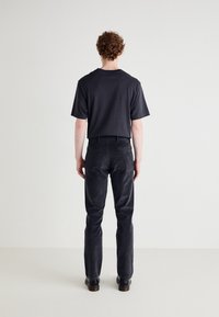 T-shirt en coton noir et pantalon en velours côtelé gris foncé vus de derrière, présentant une coupe décontractée et un design droit. Chaussures noires visibles.