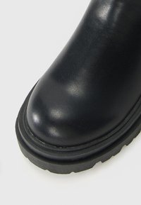 Schwarze Lederstiefel mit abgerundetem Zehenbereich und dicker Profilsohle auf einem weißen Hintergrund.