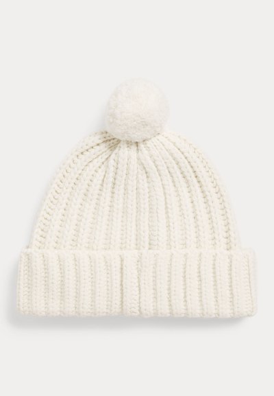 Witte gebreide wintermuts met omgeslagen rand en een pluizige pompon bovenop, getoond tegen een effen lichte achtergrond.
