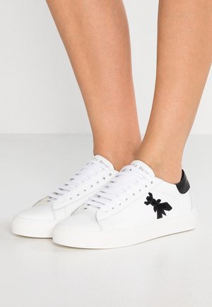 Bílé kožené tenisky s černými patními akcenty, plochými tkaničkami a výrazným černým logem mašle na boku. Hladká textura a minimalistický design.