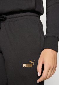 Zwarte sweatpants met een gestructureerde afwerking, voorzien van een gouden Puma-logo op het linkeronderbeen en een elastische tailleband met een trekkoord.