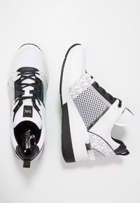White athletic sneakers with black accents, featuring a mesh upper, textured side panel, and black laces. Logo on tongue and side.