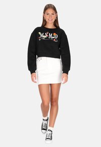 Fekete, rövid fazonú pulóver színes virágos hímzéssel, fehér farmer miniszoknyával és fekete magas szárú tornacipővel párosítva.