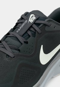 Schwarzer Sportschuh mit Mesh-Obermaterial, weißem Nike-Logo, grauen Akzenten, strukturiertem Oberflächenfinish und Schnürdesign mit stabilisierenden Elementen.