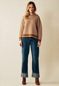 Brun mönstrad tröja med boxig passform, ribbade muddar och nederkant, tillsammans med högmidjade blå jeans med uppvikt nederkant.