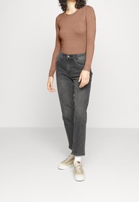 Haut marron à manches longues côtelé associé à un jean taille haute gris foncé et des baskets beiges. La tenue présente une silhouette ajustée et un tissu texturé.
