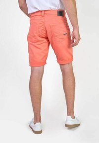 Koraalkleurige shorts met een opgerolde zoom, gemaakt van textuurstof. Heeft twee achterzakken en een logopatch op de tailleband. Gemaakt met witte schoenen.