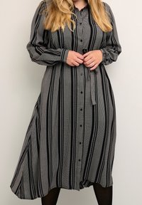Svartvit randig skjortklänning med knäppning fram, långa ärmar och midjeband. Har en flödande A-linjeform och lättviktsmaterial.
