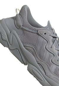 Sneaker grigio con tomaia in mesh e accenti in suede. Suola testurizzata con motivo a onde e lacci regolabili per una vestibilità sicura.