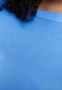 Tissu bleu clair côtelé avec une finition texturée. L'encolure présente un design arrondi, mettant en valeur la surface lisse de la chemise.