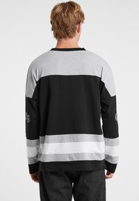 Långärmad skjorta med horisontella ränder i svart, grått och vitt. Tillverkad av mjuk bomull med rund halsringning och logodetalj på ärmen.