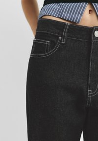 Jeans in denim nero con cuciture bianche, caratterizzati da una vita media, tasche anteriori e chiusura con bottone. La texture sembra robusta.
