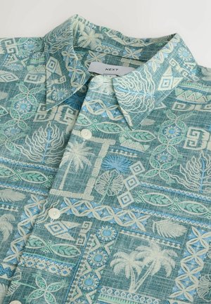 Trumpomis rankovėmis marškiniai su sagomis, turkio ir mėlynos spalvos tropiniais geometriniais raštais ir palmių motyvais, sulankstyti taip, kad matytųsi apykaklė ir sagos.