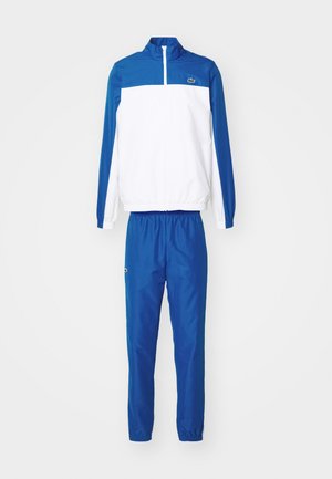 Chándal azul y blanco hecho de tejido ligero; chaqueta con cremallera y cuello alzado, y pantalones con cintura elástica; logotipo en la chaqueta.