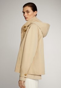 Beige hoodie met een relaxte pasvorm, voorzien van grote knopen, zijzakken en een soepele textuur. Ontworpen voor casual gebruik.