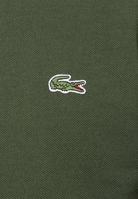 Grön stickad skjorta med en liten broderad krokodillogo i grönt och rött på vänster bröst.