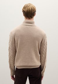 Maglione a trecce in beige chiaro con collo alto, polsini e orlo a coste. Presenta maniche con motivo intrecciato.