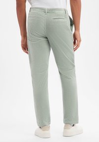 Ανοιχτό πράσινο παντελόνι κοτλέ με σχεδίαση ίσιας γραμμής, διαθέτει πίσω τσέπες και λεία υφή. Συνδυάζεται με λευκά αθλητικά παπούτσια.