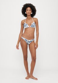 Baltas maudymosi kostiumas su mėlynomis gėlių raštais, trikampio formos viršus su kaklo dirželiais ir atitinkančios maudymosi kelnaitės. Lygus audinio paviršius.