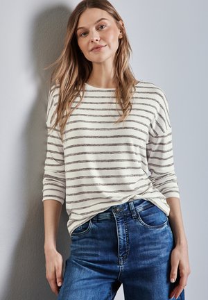 Camisa de manga larga a rayas en crema y marrón, combinada con jeans de denim azul. La camisa tiene un corte holgado y puños acanalados.