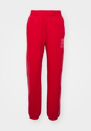 Pantalons de survêtement rouges avec taille élastique, jambes fuselées, rayures blanches sur les côtés et une petite étiquette de logo à l'avant. Tissu au toucher doux.