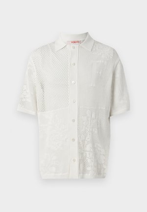 Bela kratka polo majica s kratkimi rokavi s teksturiranim pletenim dizajnom, ki ima izrazite panele iz mrežastega materiala in cvetlične vzorce, ter sprednje gumbno zapiranje.