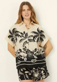 Korte mouwen shirt in crème met zwart tropisch bloemenpatroon, met een knoopsluiting aan de voorkant en een relaxte pasvorm; bijpassende zwarte shorts met een vergelijkbaar patroon.