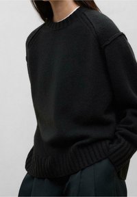 Pull noir en maille avec un col et un ourlet côtelés. Présente une coupe décontractée et des coutures d'épaule tombantes. Texture douce, design minimaliste.