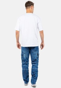 T-shirt en coton blanc à manches courtes porté avec un pantalon cargo en denim bleu, doté de poches latérales, d'une coupe droite et d'une texture décolorée.