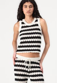 Fekete-fehér csíkos kötött crop top fodros széllel, párosítva hozzá illő nadrággal, amely húzózsinórral rendelkezik és nyitott öltésmintával készült.